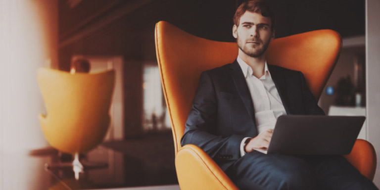Man sitting in an orange armchair working on his laptop.